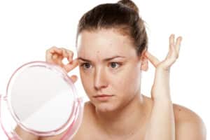 Young female tucking her ears in front of a mirror considering otoplasty surgery for herself.