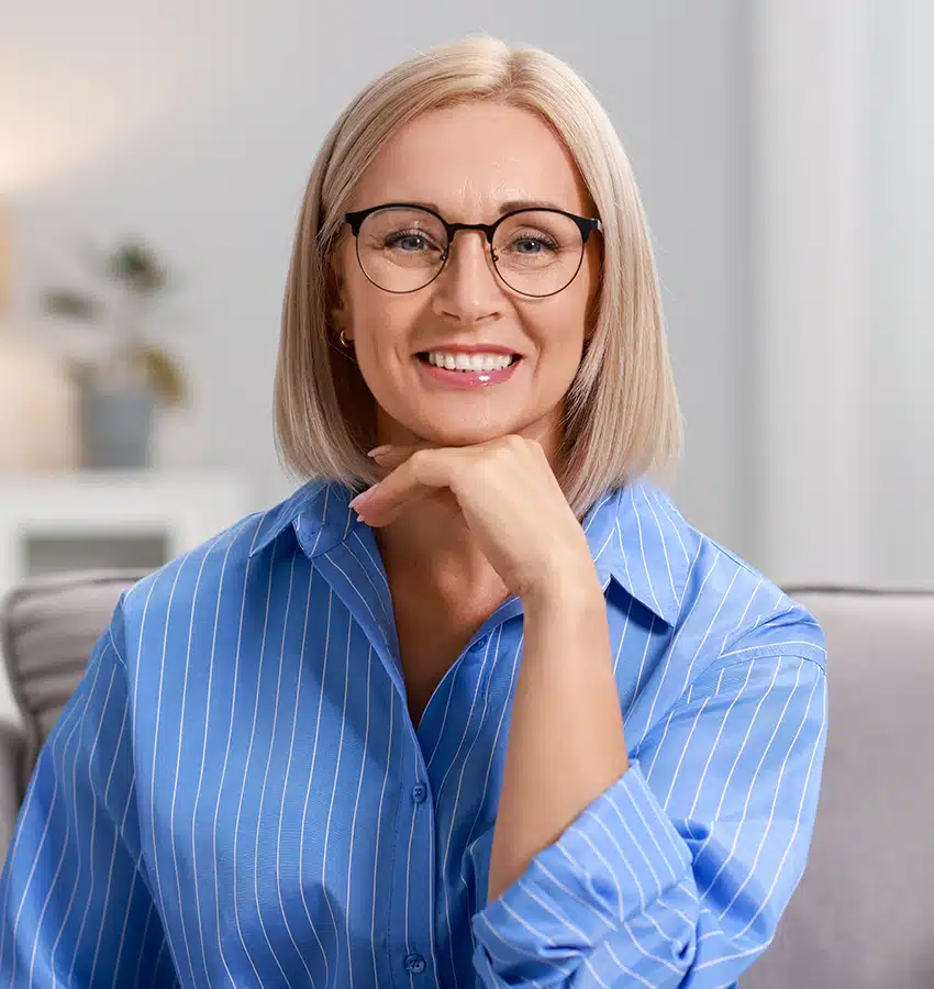 Smiling middle-aged woman with glasses and smooth skin, showing mini facelift results around jawline and cheeks