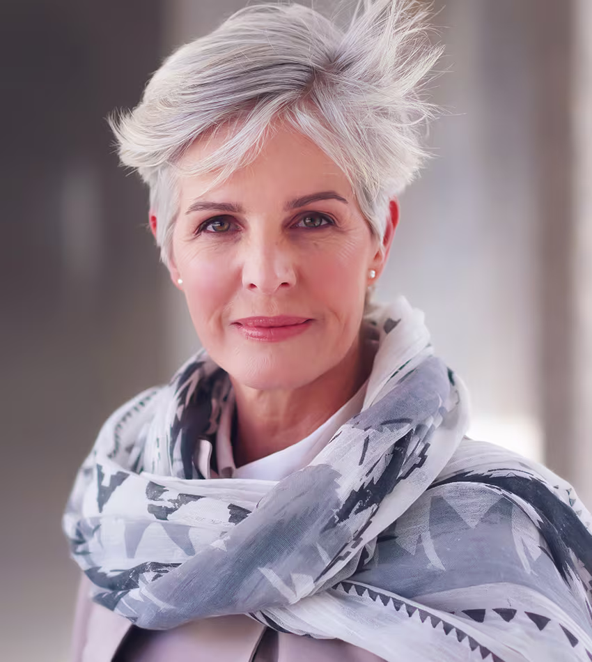 Confident older woman with short gray hair and scarf, showing natural facelift results with youthful appearance.