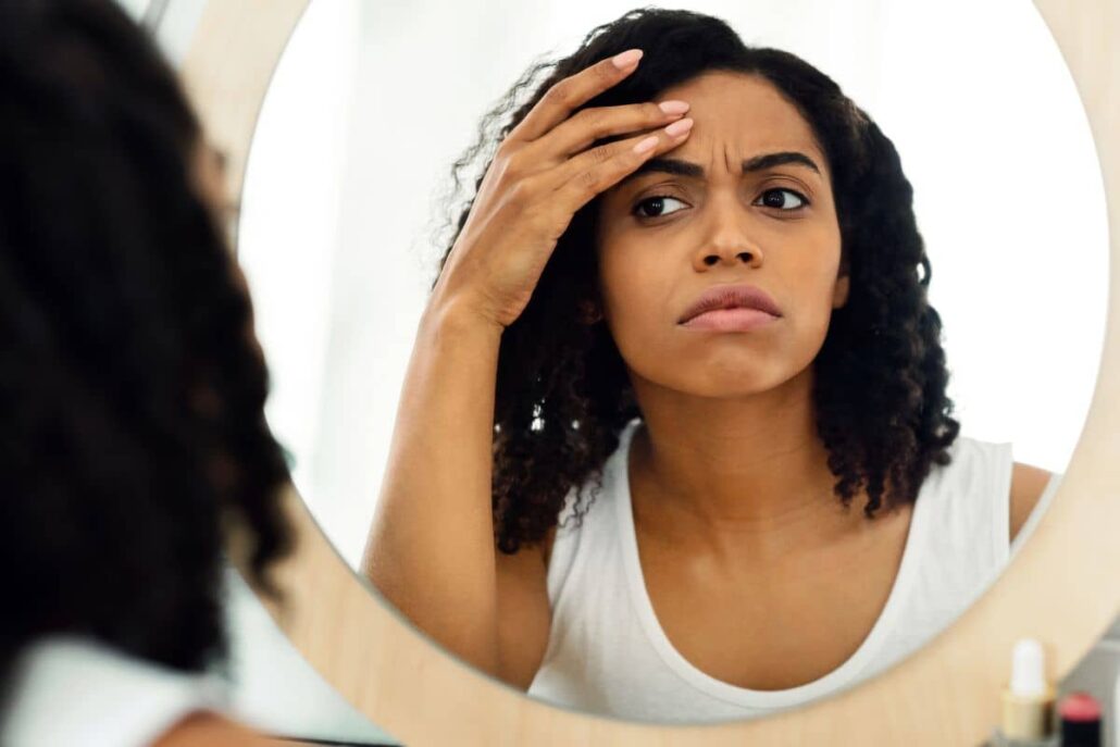 Woman examining forehead lines in mirror, highlighting common Botox treatment areas like frown lines and forehead wrinkles.