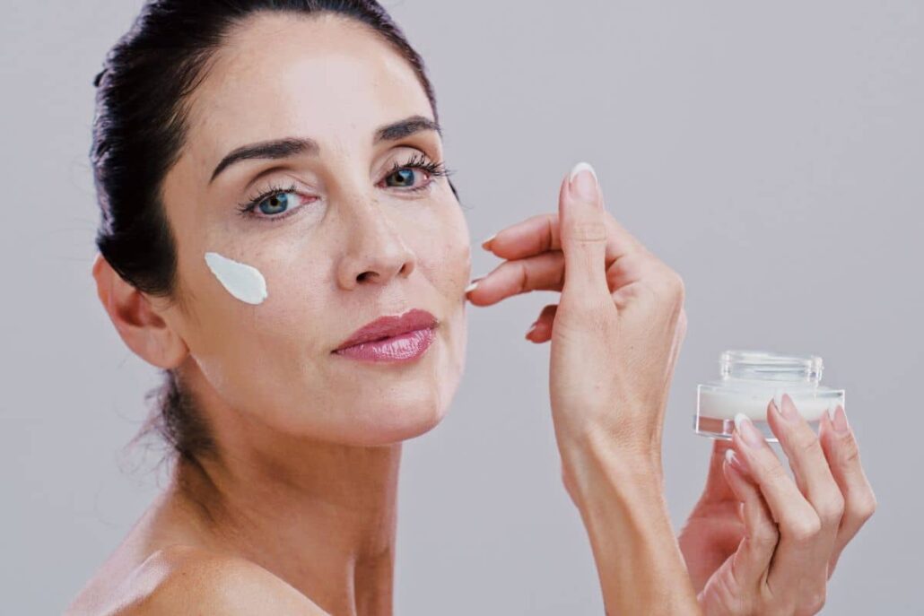 Woman applying cream to her face as part of a skincare routine to maintain deep plane facelift longevity