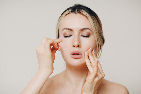 Woman touching facial skin to demonstrate loss of skin elasticity and visible signs of aging on the face.