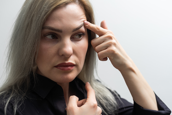 Woman pointing at forehead to illustrate gravity-related facial sagging and jowl formation over time.