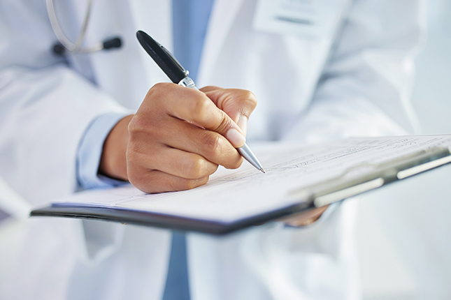 Doctor in a white lab coat filling out medical patient registration forms on a clipboard.