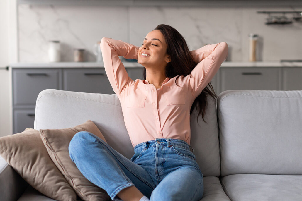 Woman relaxing on couch at home during rhinoplasty recovery period, representing comfort and healing process.