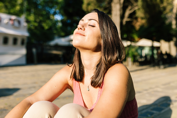 Woman sitting outdoors in sunlight to represent sun exposure, collagen breakdown, wrinkles, and skin damage.
