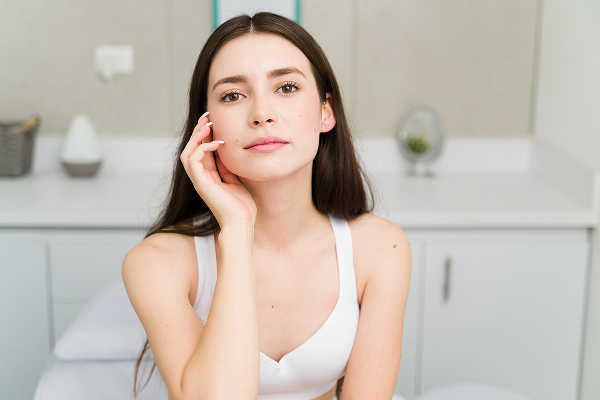Woman touching her face to illustrate facial volume loss, flatter cheeks, and heavier lower face appearance.