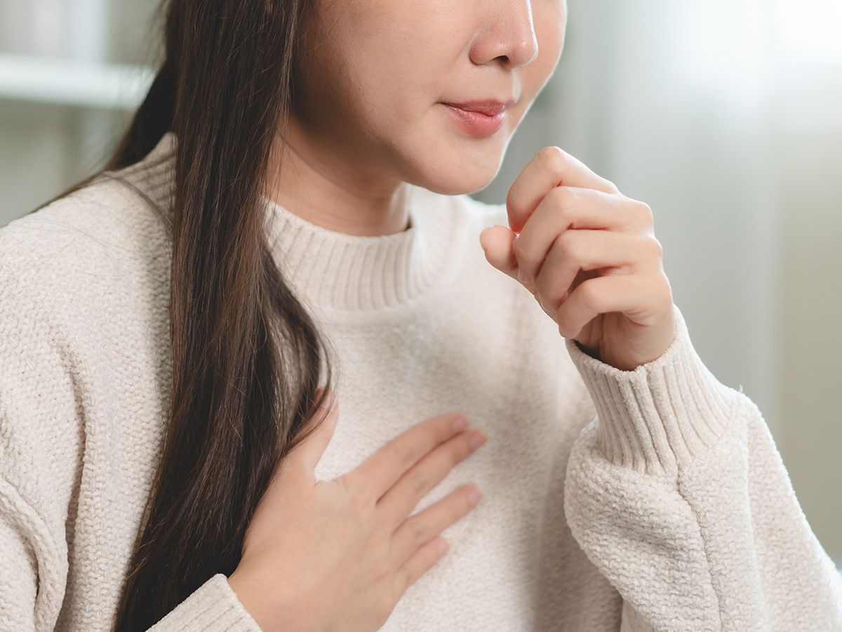 Woman experiencing cough and chest discomfort illustrating symptoms of allergies and asthma affecting breathing.