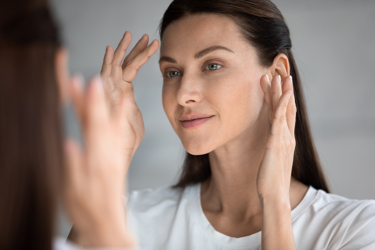 Woman touching face in mirror showing smoother, slimmer facial contours after facial liposuction.