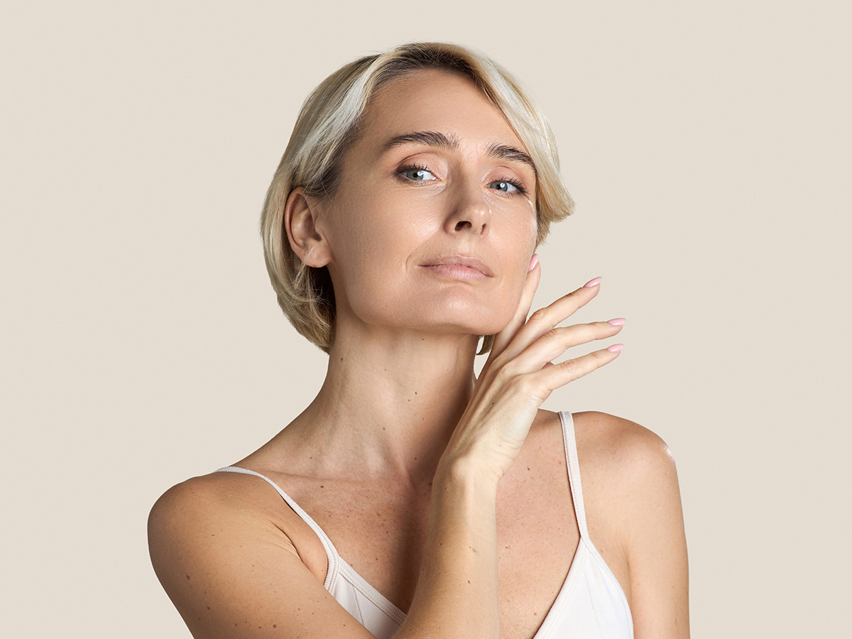 Mature woman touching her face, representing ideal candidate for facial fat transfer and wrinkle reduction