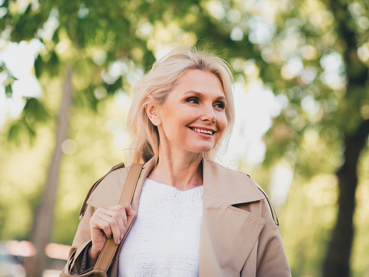 Mature woman smiling outdoors with smooth skin, representing Jeuveau treatment for reducing dynamic facial wrinkles