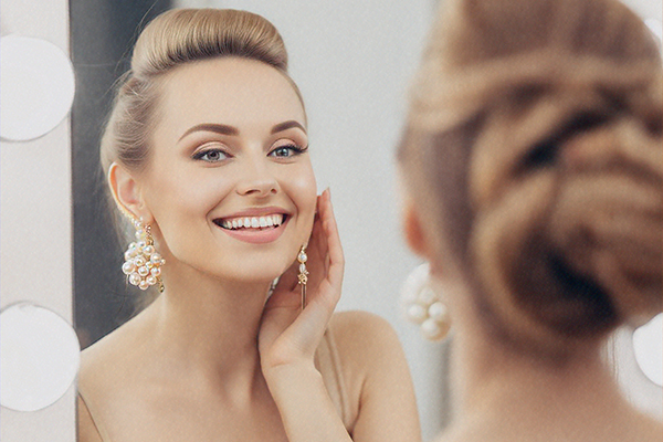 Woman smiling at mirror with improved ear symmetry after otoplasty procedure