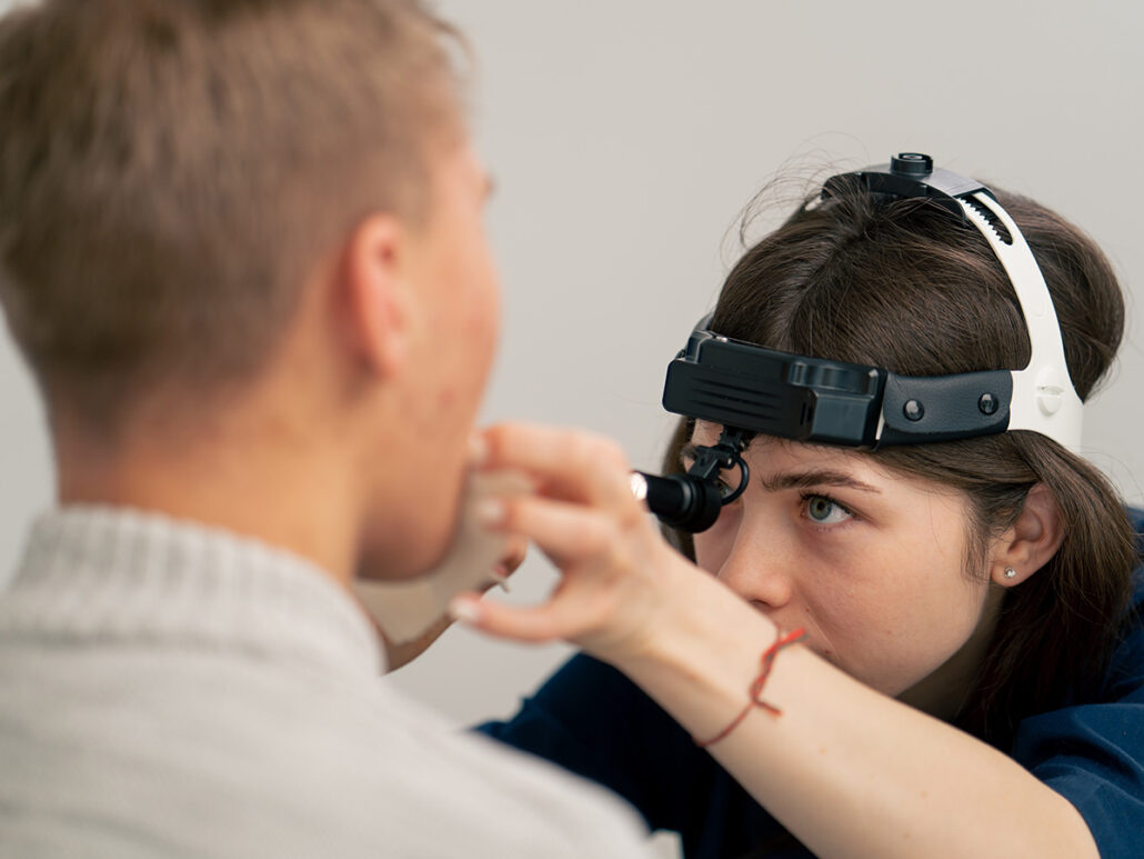 Doctor examining patient throat to diagnose voice, swallowing, or reflux-related ENT conditions.