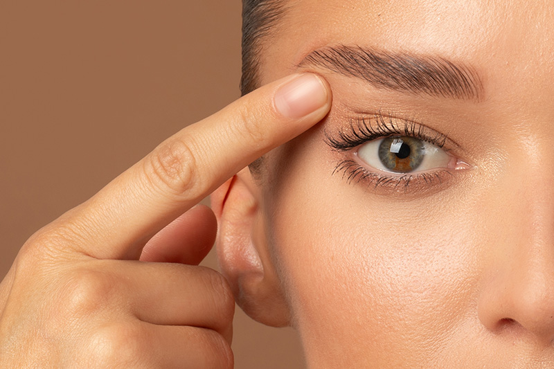 Close-up of eye with finger lifting upper eyelid skin, showing smoother contour after upper blepharoplasty