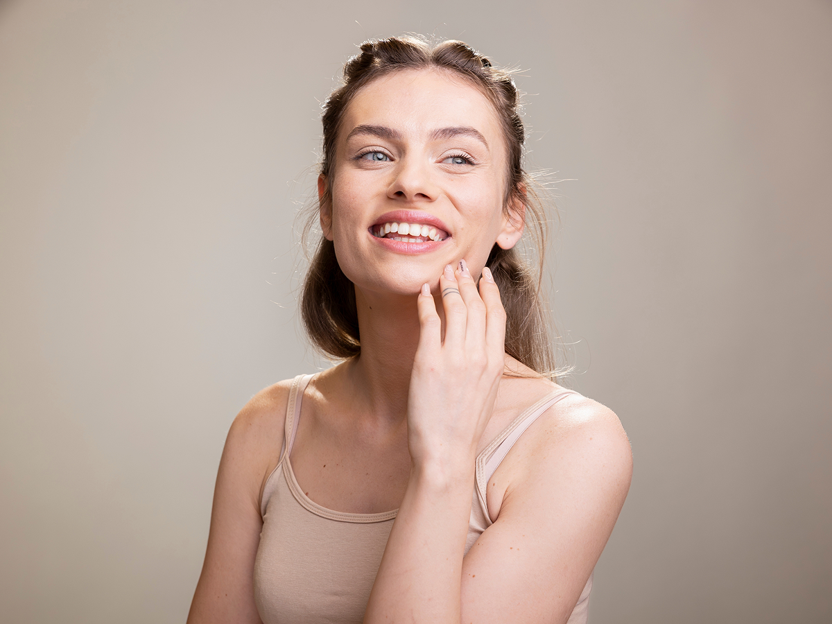 Woman smiling and touching cheek illustrating Voluma facial filler safety and natural-looking results