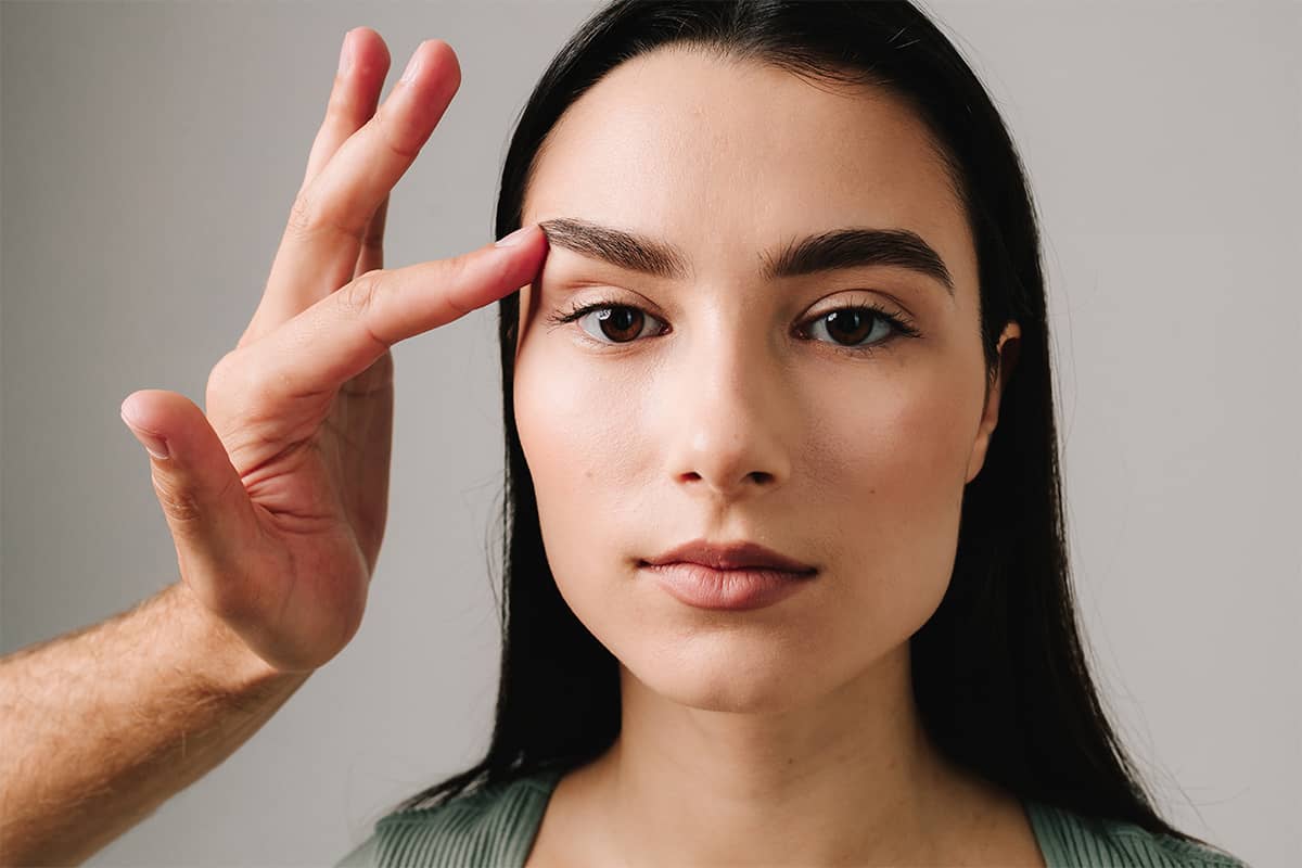A close-up of a woman’s face while a practitioner’s hand gently lifts her brow to assess eyelid laxity and field of vision.
