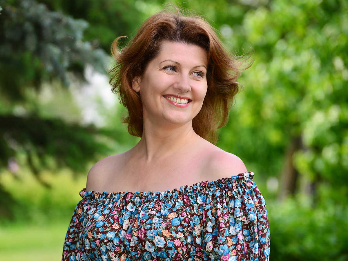 Smiling woman outdoors representing blepharoplasty surgery for drooping eyelids.