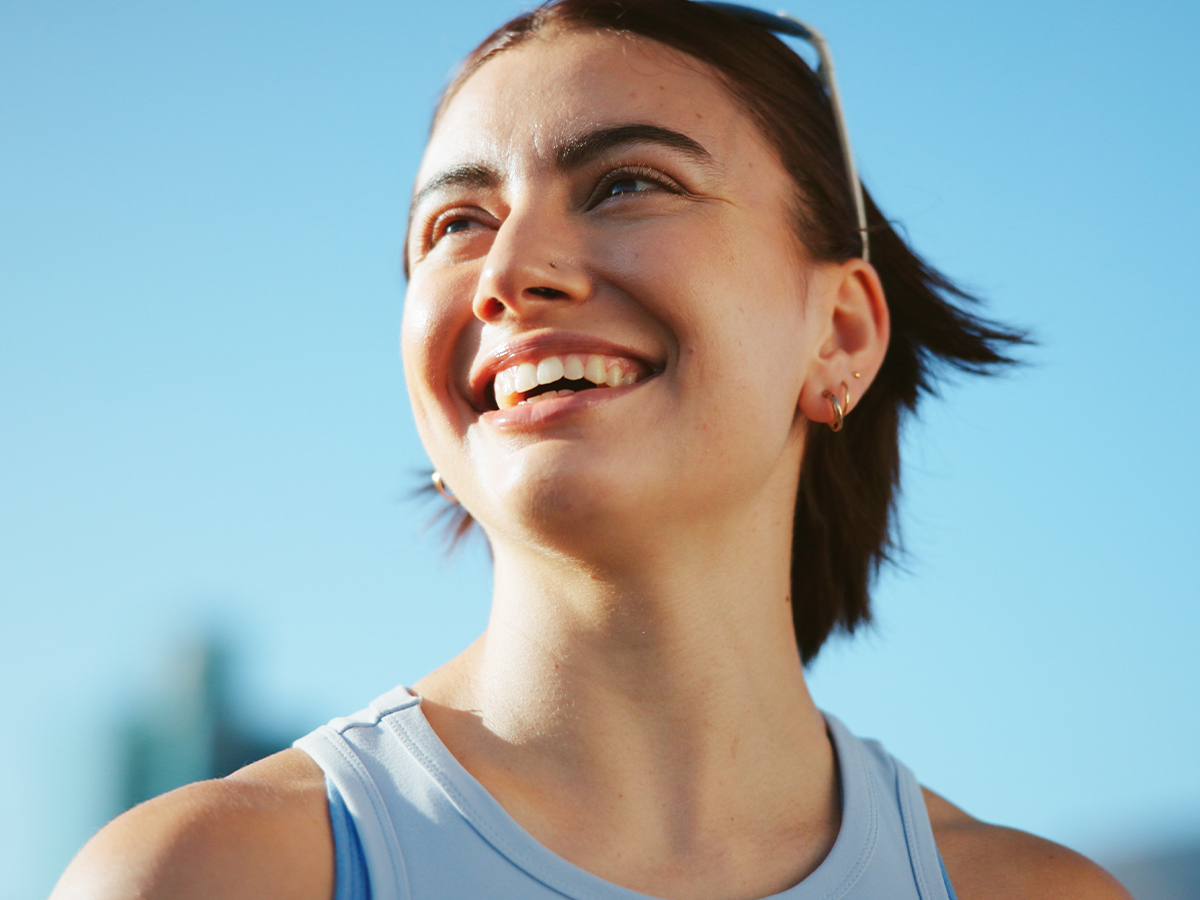Smiling woman outdoors representing rhinoplasty improvements for nasal shape, profile, and breathing function.
