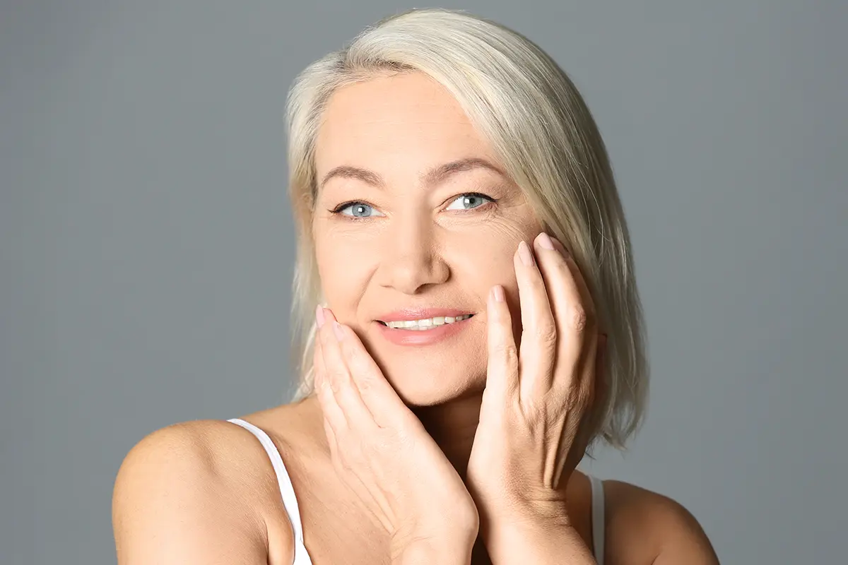 Mature woman touching her face after skin rejuvenation treatment.